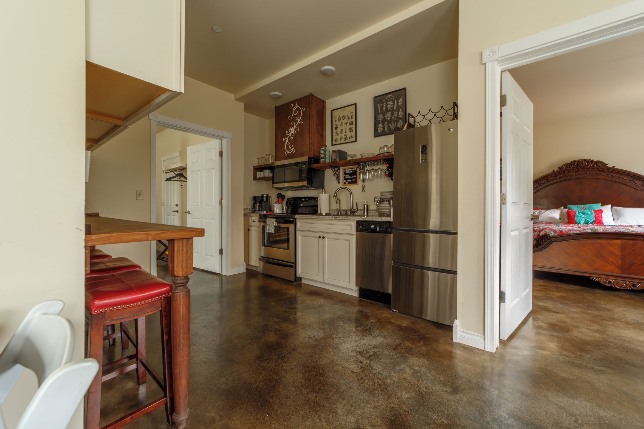 A spacious kitchen with modern appliances, a dining area with a red leather bench, and a bedroom with a wooden headboard.