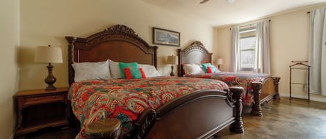 Cama doble con dos mesas de noche con lámparas, ventilador de techo y ventana con cortinas.