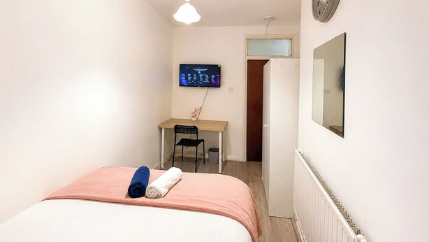 Ein Schlafzimmer mit Bett, Schreibtisch, Stuhl, Fernseher und Heizkörper.