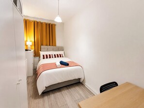 Ein Hotelzimmer mit Bett, Nachttisch, Lampe und Holztisch.