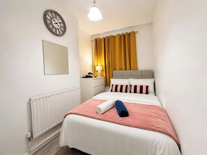 Ein Hotelzimmer mit Bett, Nachttischlampe, einer Uhr und einem Fenster mit Vorhängen.