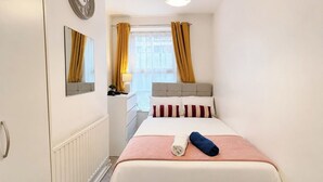 Ein Hotelzimmer mit einem Bett, einem Nachttisch, einem Spiegel, einem Fenster mit Vorhängen und einer Wanduhr.
