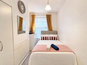 Ein Hotelzimmer mit einem Bett, einem Nachttisch, einem Spiegel, einem Fenster mit Vorhängen und einer Wanduhr.