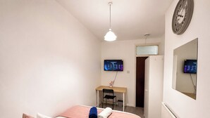 Ein Schlafzimmer mit einem Bett, einem Schreibtisch, einem Stuhl und zwei Monitoren an der Wand.