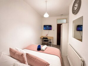 Ein Schlafzimmer mit einem Bett, einem Schreibtisch, einem Stuhl und zwei Monitoren an der Wand.