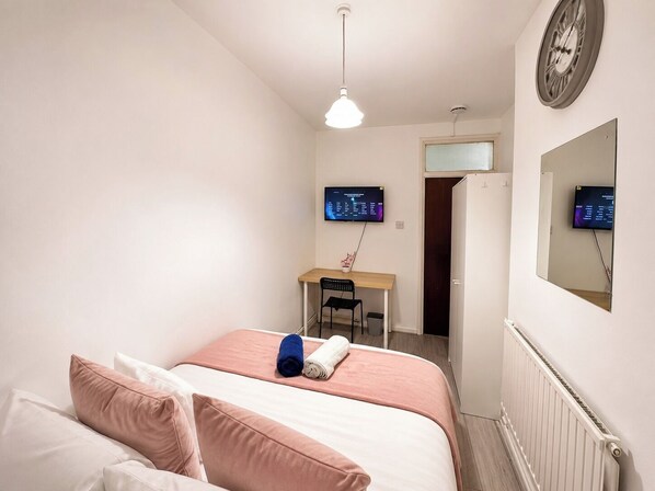 Quarto com cama, escrivaninha, cadeira e dois monitores na parede.