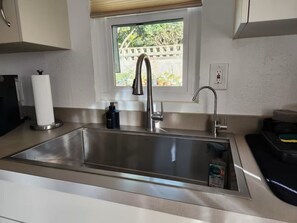 Eine Spüle aus Edelstahl mit modernem Wasserhahn, ein Fenster darüber und eine Küchenrolle auf der Arbeitsplatte.
