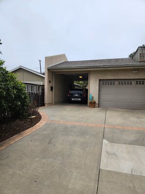 Eine Garage mit einem Auto darin, eine Auffahrt, die zur Garage führt, und ein kleiner Gartenbereich mit einem Kaktus.
