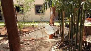 A hammock suspended between trees in a garden area with a building in the background.