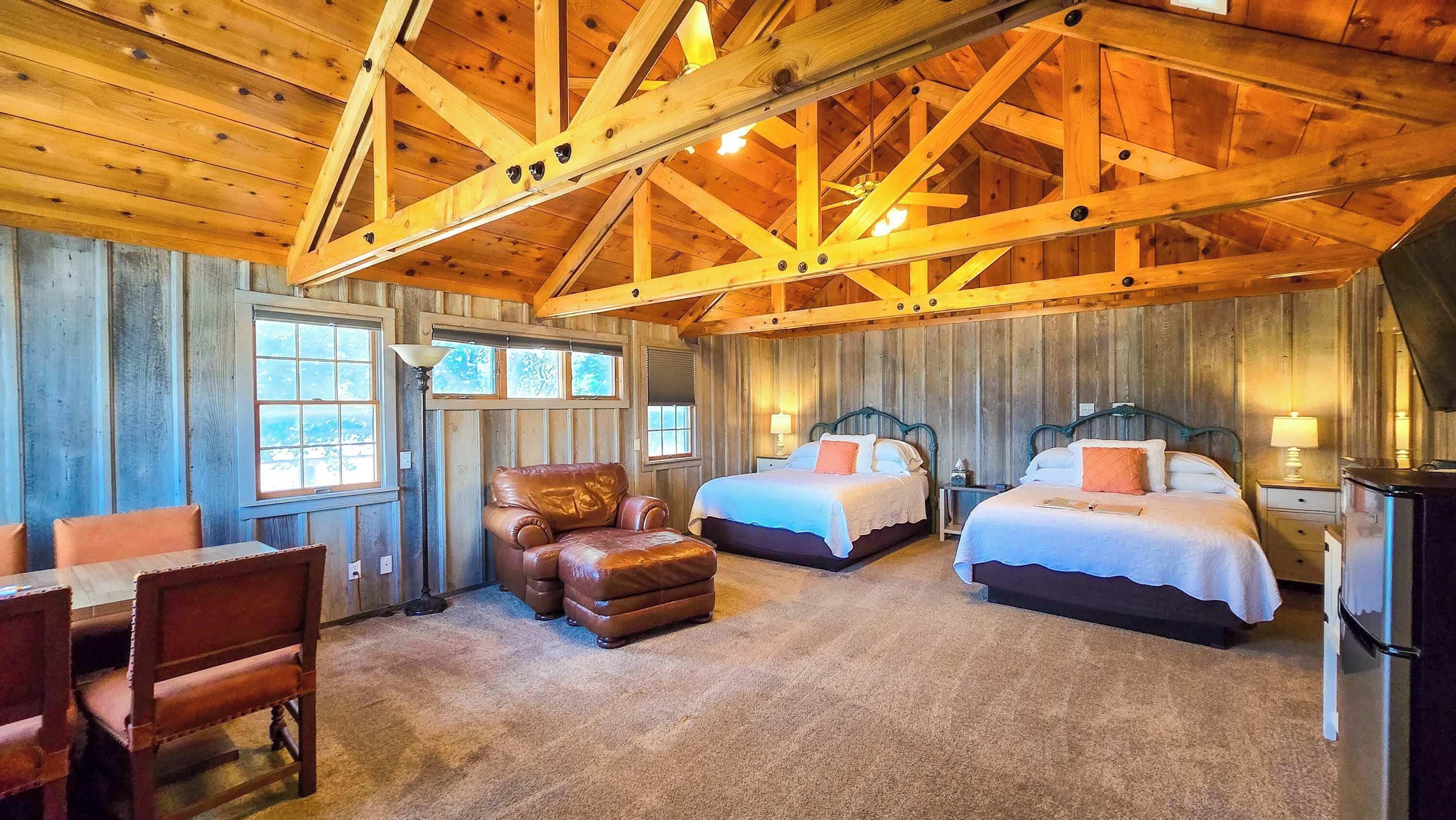 L’intérieur d’un chalet en bois comprend deux lits, un fauteuil en cuir et un coin repas.