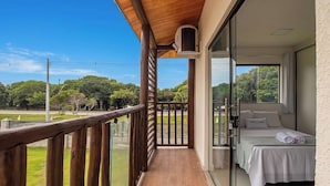 Un balcon avec une balustrade en bois, un lit recouvert d’une courtepointe blanche et une vue sur des arbres et une route.