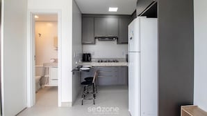 Une cuisine compacte avec des meubles gris, un réfrigérateur blanc et un petit coin repas équipé d’une chaise.