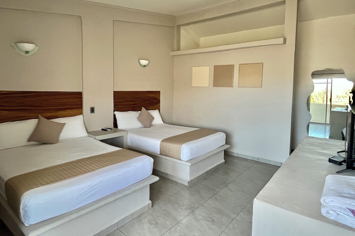 A hotel room with two beds, a desk, and a mirror.