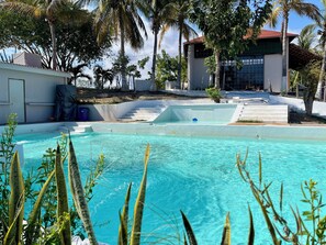 A swimming pool with clear water, surrounded by palm trees and a building with a red roof. - Hotel Mare (Santa Maria Huatulco)