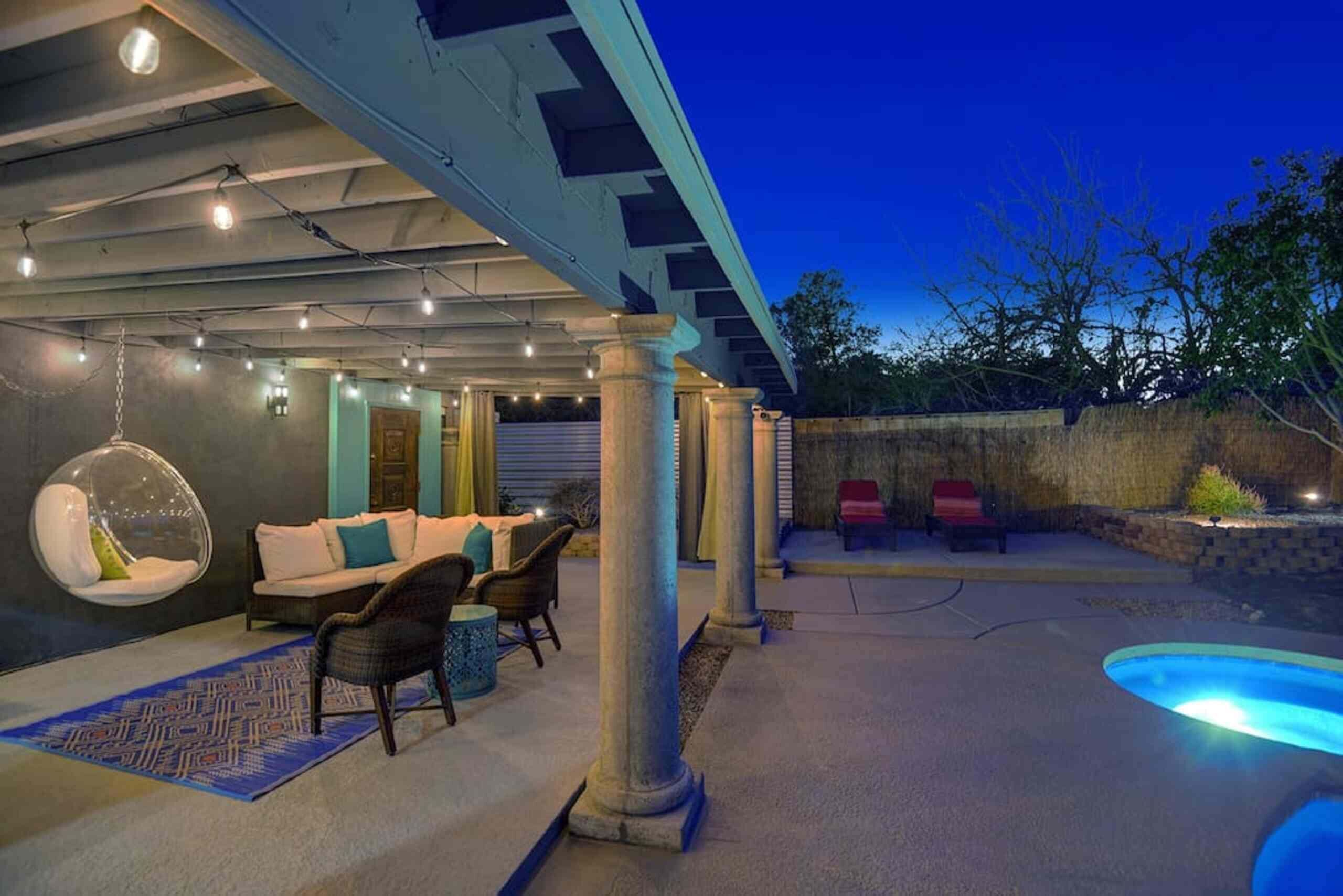 An outdoor patio area with a hanging chair, seating, and a pool.