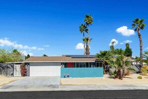 A single-story house with a garage, a small attached structure with a blue facade, and a clear blue sky. - Navigate Stays Pool, Spa & Pet-Friendly PS Home (Palm Springs)