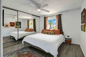 A bedroom with two beds, a ceiling fan, a large mirror, and a view of the outdoors. - Navigate Stays Pool, Spa & Pet-Friendly PS Home (Palm Springs)