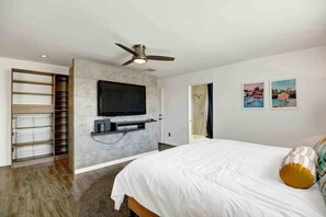 Ein Schlafzimmer mit einem Bett, einem an der Wand befestigten Fernseher, einem Deckenventilator und einer Tür zu einem Badezimmer.