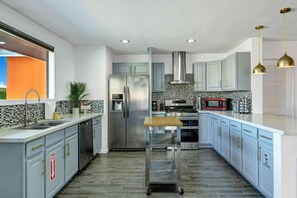 A modern kitchen with stainless steel appliances, a central island, and light blue cabinetry. - Navigate Stays Pool, Spa & Pet-Friendly PS Home (Palm Springs)