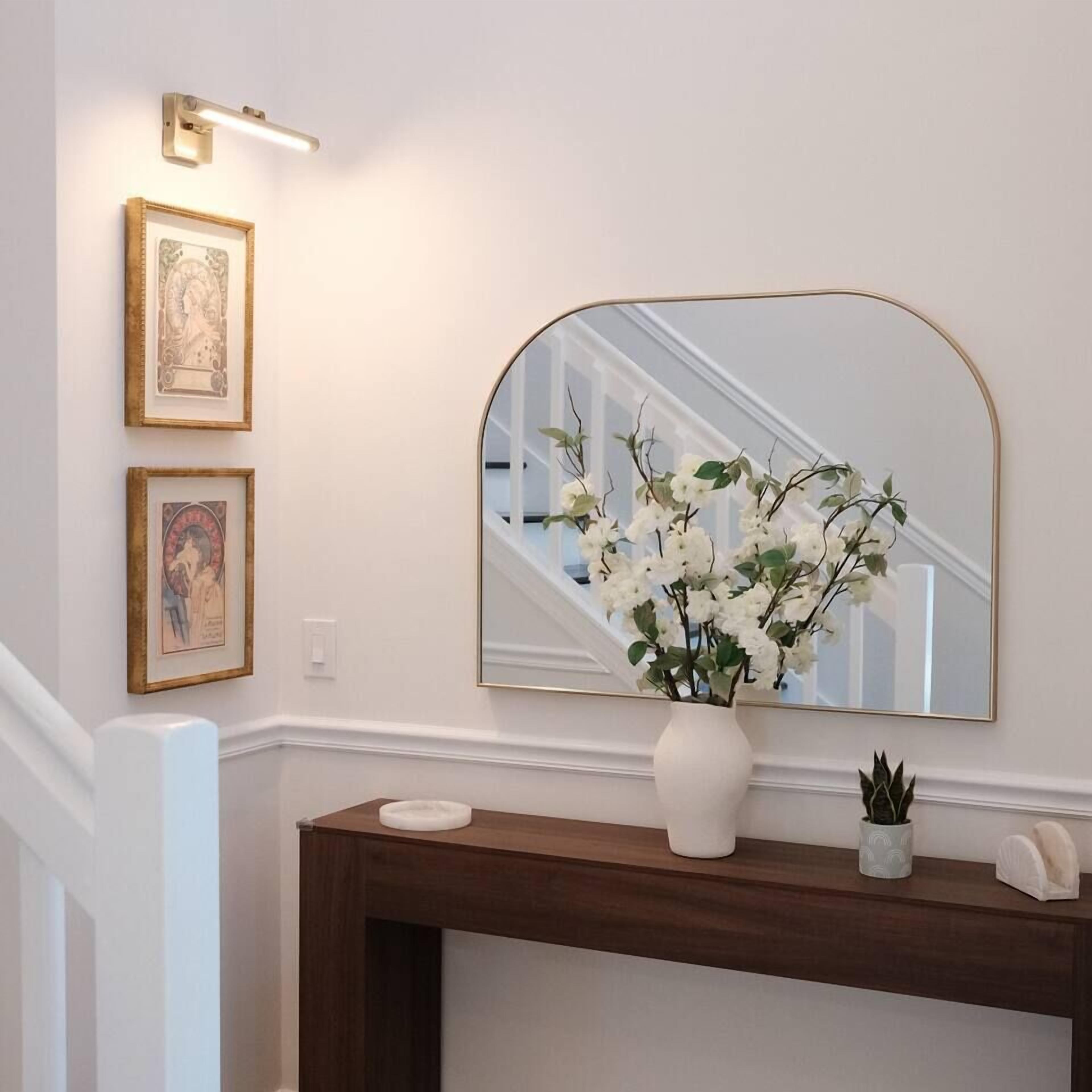A hallway with a mirror, a vase with flowers, and two framed pictures on the wall.