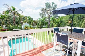 A poolside area with a wooden deck, a table with chairs, and a large umbrella. - Treasure Coast Villa 5bd + pool hot tub game room (Port St. Lucie)