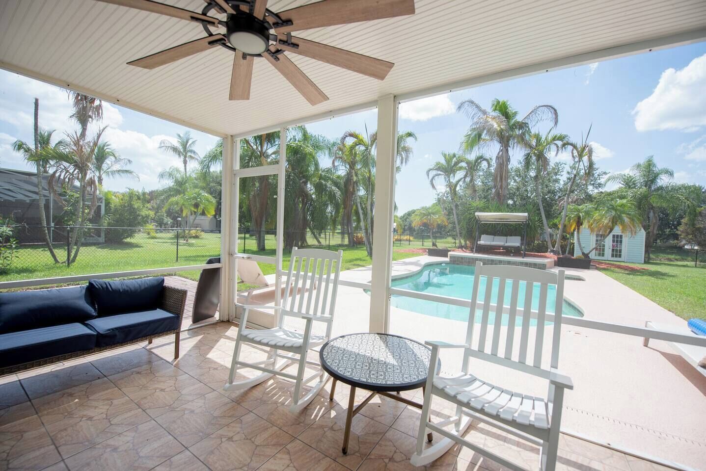 A covered patio area with a pool, outdoor furniture, and a view of a residential neighborhood.