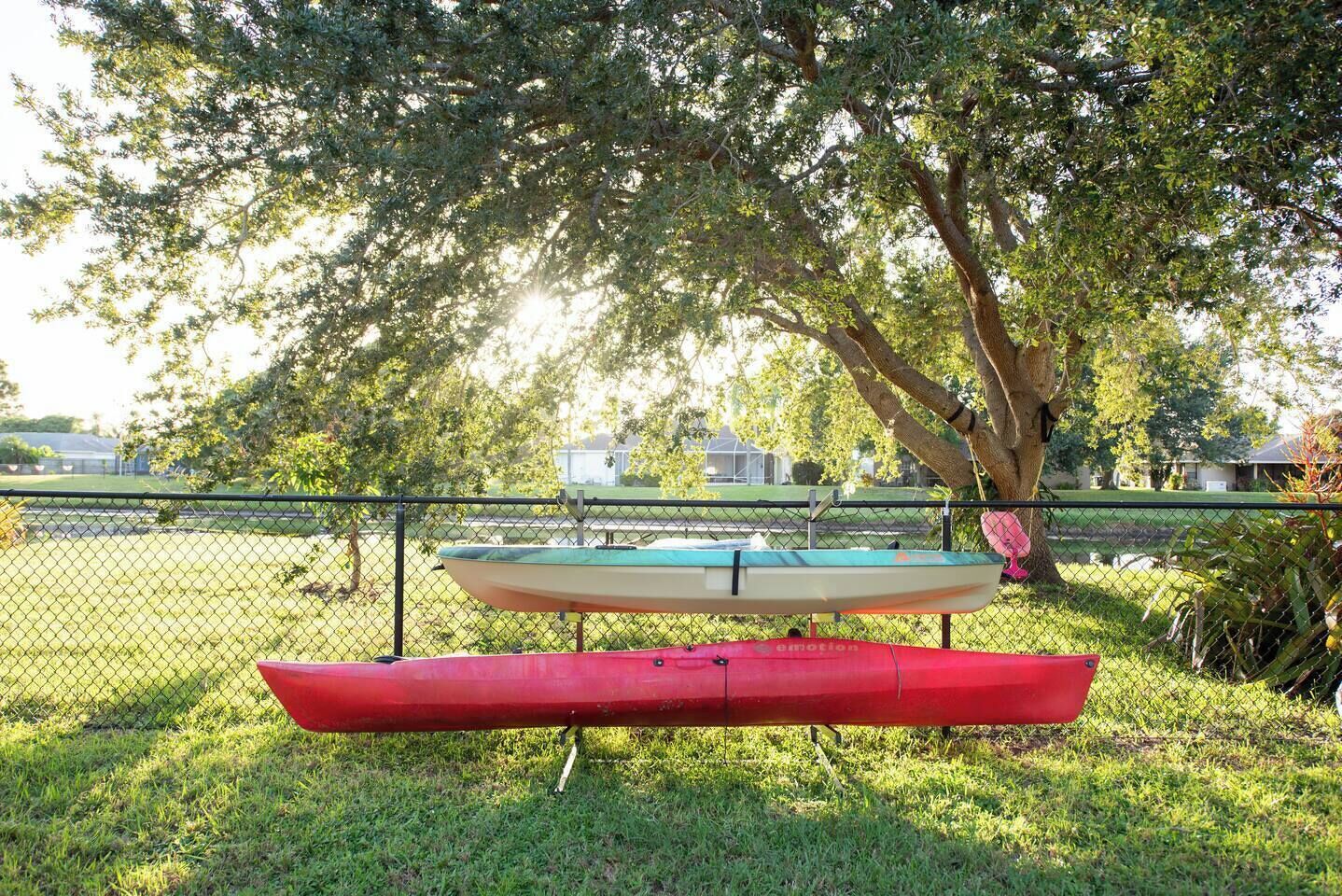 Un espace délimité par une clôture, avec deux canoës, l’un rouge et l’autre vert, à l’ombre d’un arbre.