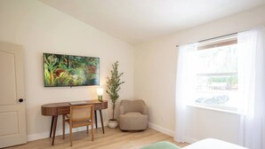 Ein Zimmer mit einem Bett, einem Schreibtisch mit Stuhl, einer Pflanze und einem Fenster mit Vorhängen.