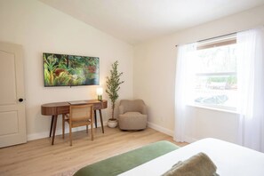 Ein Zimmer mit einem Bett, einem Schreibtisch mit Stuhl, einer Pflanze und einem Fenster mit Vorhängen.