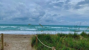 Ein Strand mit einem Holzsteg, der zum Wasser führt, umgeben von Gras und einem bewölkten Himmel.
