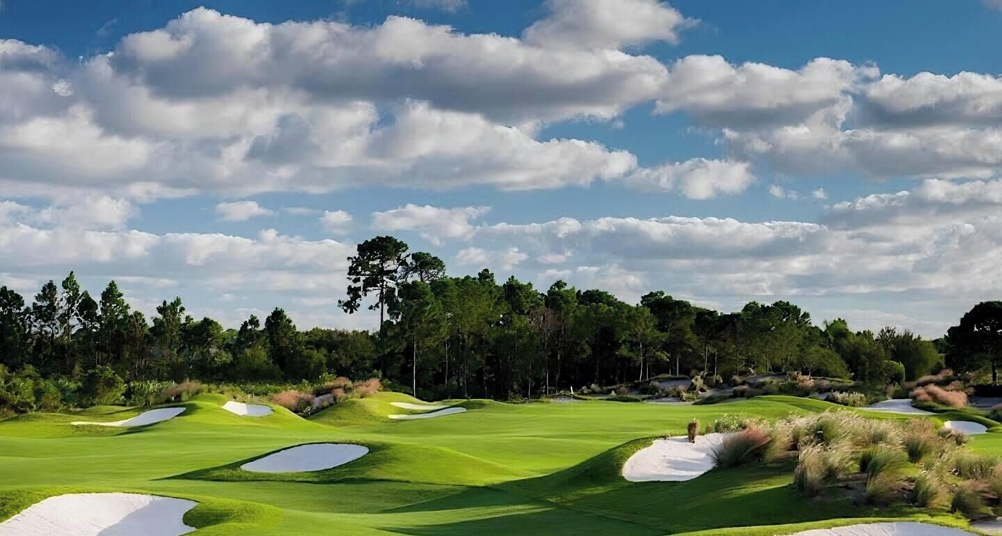 A golf course with sand bunkers, trees, and a clear sky.