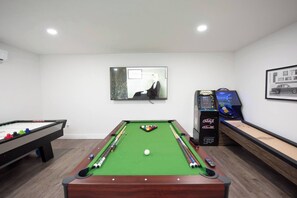 A pool table with balls and cues, a billiard table, and a video game machine.