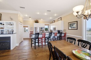 A spacious kitchen with white cabinets, a wooden dining table, and a view of the outdoors. - Beachfront Luxury | Pool, Hot Tub, Elevator (Saint George Island)