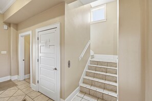 A hallway with a white door, a small window, and a staircase with beige tiles. - Beachfront Luxury | Pool, Hot Tub, Elevator (Saint George Island)