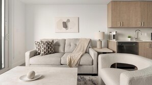 Ett modernt vardagsrum med en soffa, fåtölj, soffbord och en matplats med en lampa och en kaffemaskin.
