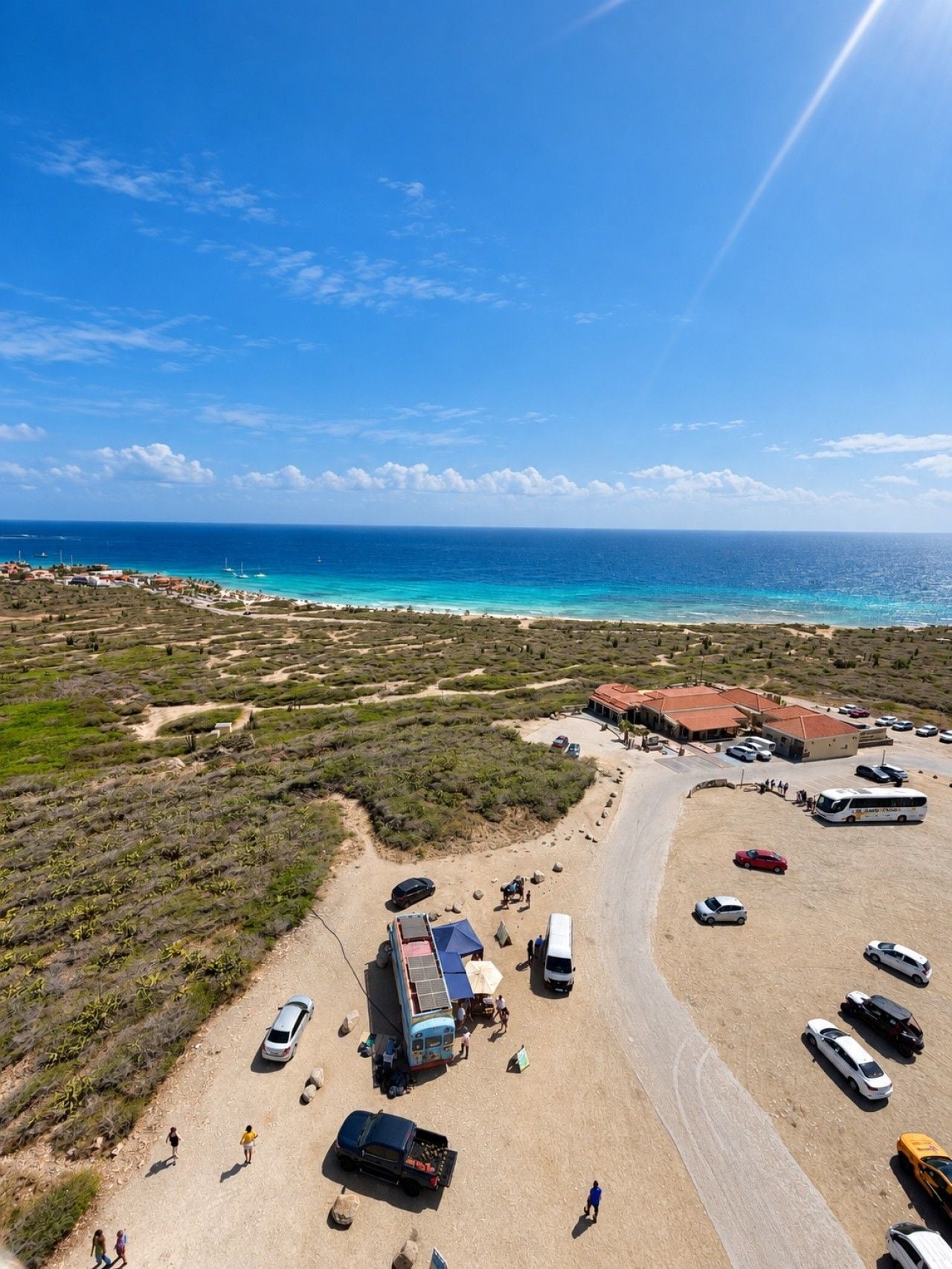 An aerial view of a coastal area with a parking lot, beach, and buildings.