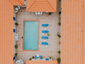 Luftaufnahme eines Poolbereichs mit Liegestühlen und Sonnenschirmen.
