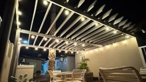 Un área de patio al aire libre con una estructura de pérgola, piso de baldosas y mobiliario exterior.