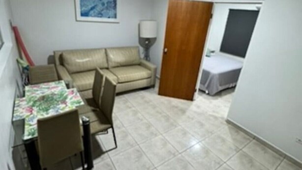 Una habitación pequeña y amoblada con un sofá, una mesa de comedor con sillas, una lámpara y una puerta que da a otra habitación.