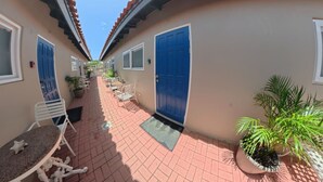 A corridor with a tiled floor, white metal chairs, a table, and potted plants. - Aruba Studio w/ Pool · King Size · Near Beach #13 (Noord)