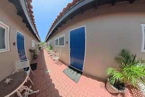 A corridor with a tiled floor, white metal chairs, a table, and potted plants. - Aruba Studio w/ Pool · King Size · Near Beach #13 (Noord)