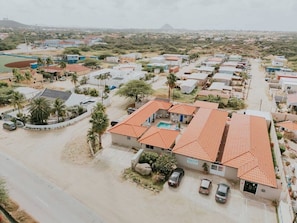 A residential area with multiple houses, a swimming pool, and a road. - Aruba Studio w/ Pool · King Size · Near Beach #13 (Noord)