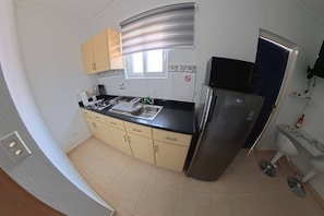 A compact kitchen with a stainless steel refrigerator, a sink, and a window with blinds. - Aruba Studio w/ Pool · King Size · Near Beach #13 (Noord)