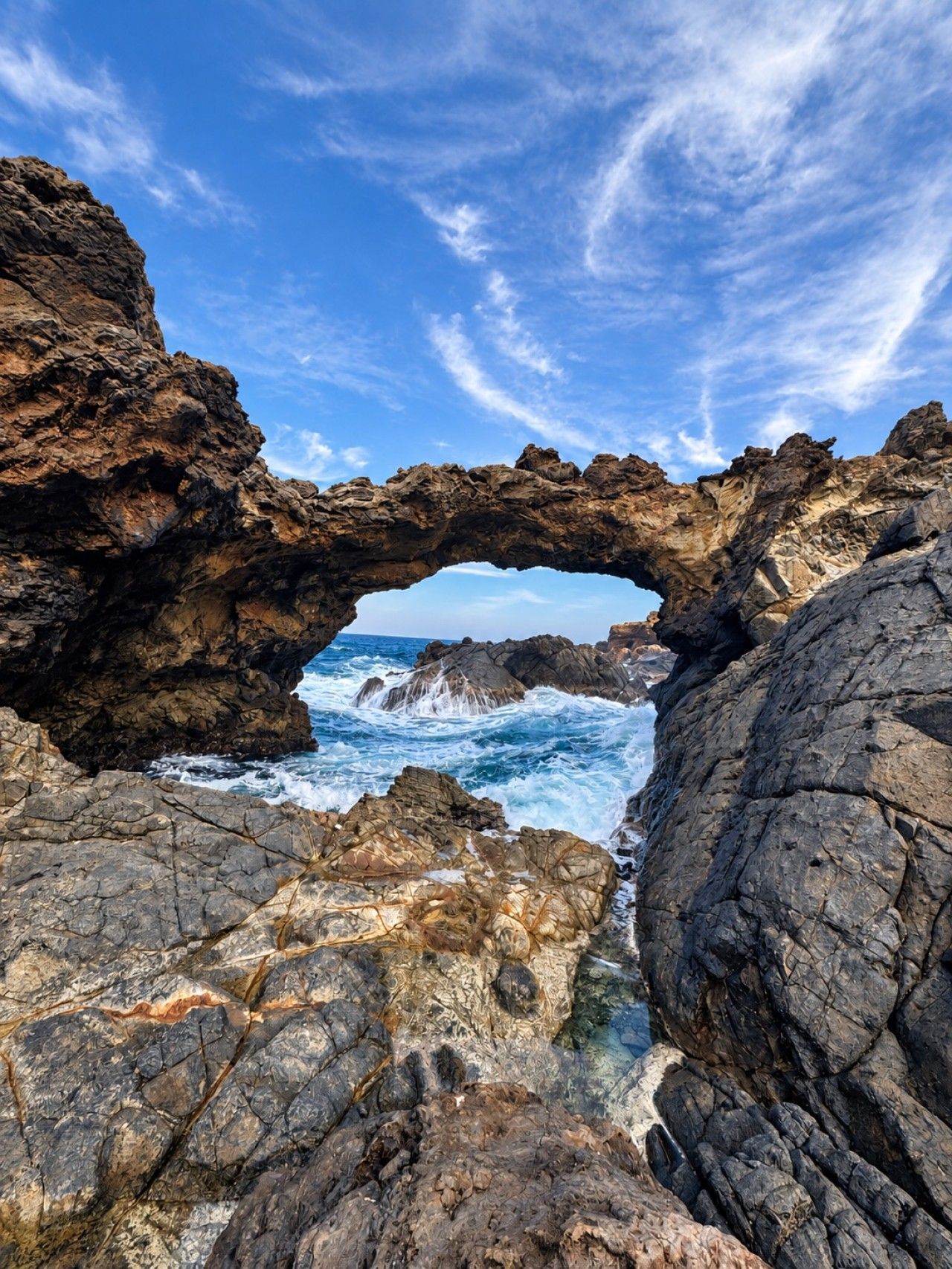 A natural rock formation with a clear view of the ocean through an arch.