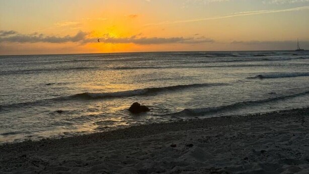 A beach scene with a sunset, waves, and a sailboat. - Aruba Studio w/ Pool · King Size · Near Beach #13 (Noord)