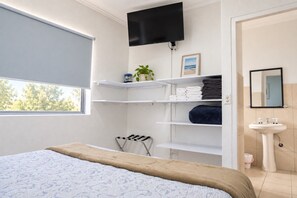 A bedroom with a bed, a TV mounted on the wall, a window, and a bathroom with a sink and mirror. - Aruba Retreat w/ Pool · King Bed · #8 (Aruba)