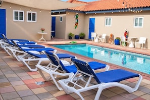 A poolside area with lounge chairs, a pool, and a building with blue doors and windows. - Aruba Retreat w/ Pool · King Bed · #8 (Aruba)