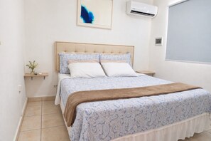 A bedroom with a bed, a bedside table, a wall-mounted air conditioner, and a window. - Aruba Retreat w/ Pool · King Bed · #8 (Aruba)