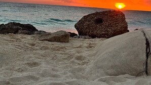 Ranta, jossa voi ihailla auringonlaskua, ja jossa on kallioisia ulokkeita sekä tyyni meri.