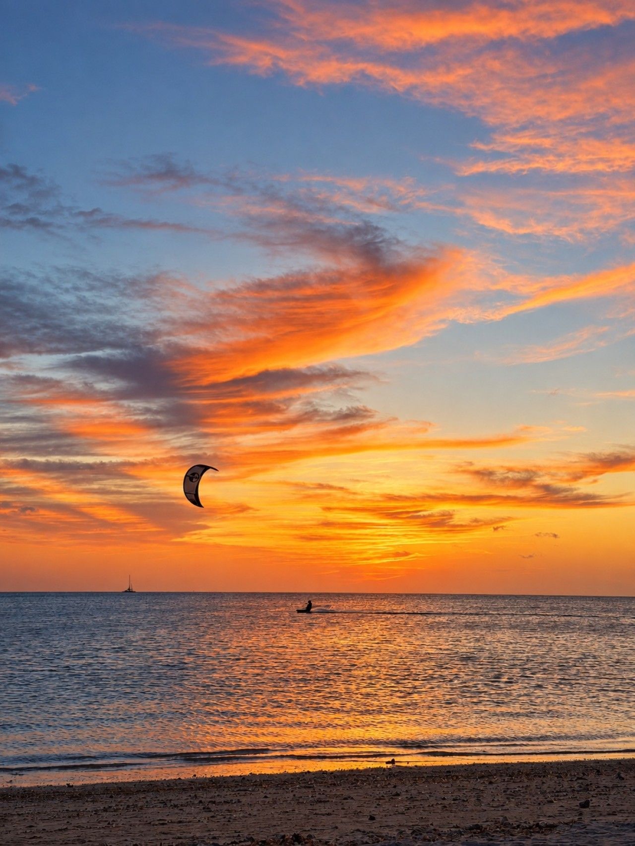 A beach scene with a sunset, a person on a paddleboard, and a sailboat in the distance.